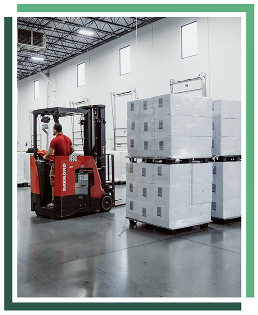 man in red shirt on a red forklift navigates between stacks of white materials inside a large warehouse
